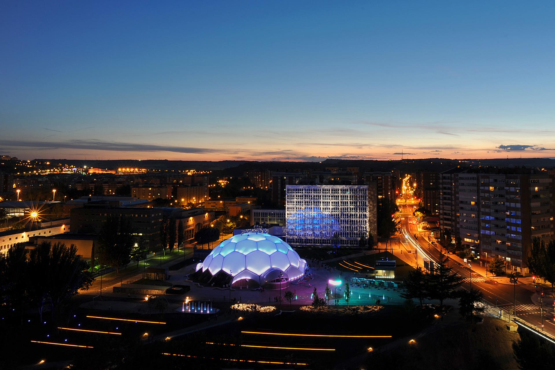 Vista aérea de la ciudad con la cúpula de la plaza milenio con fachada ETFE de noche iluminada en az