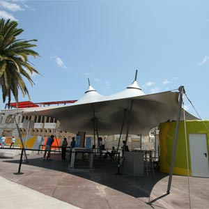 Estructura tensada en forma de carpa de circo con lona gris cubriendo equipamientos