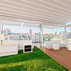 Interior de la pérgola con mobiliario blanco en tarima de madera y cesped en Hotel Oscar